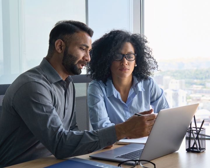 Two supply chain employees reviewing data on a laptop. 