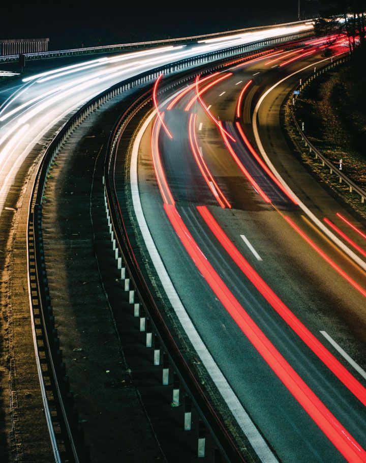 Cars on a two lane highway speeding past at night, lights blurred as they pass. 